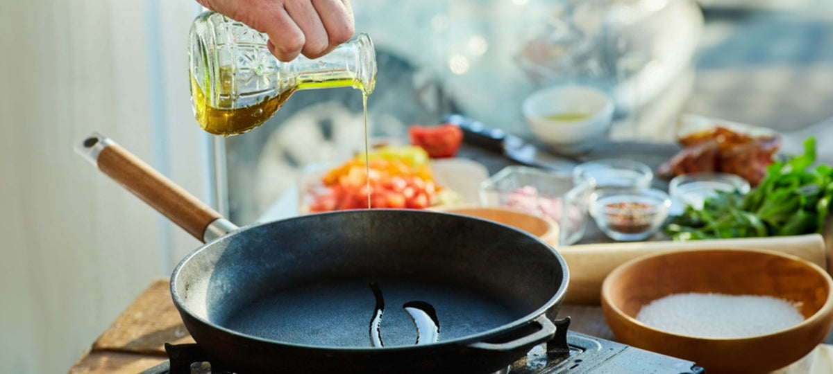 A person pouring olive oil into a frying pan while preparing ingredients to cook, exploring "Can You Fry With Olive Oil".