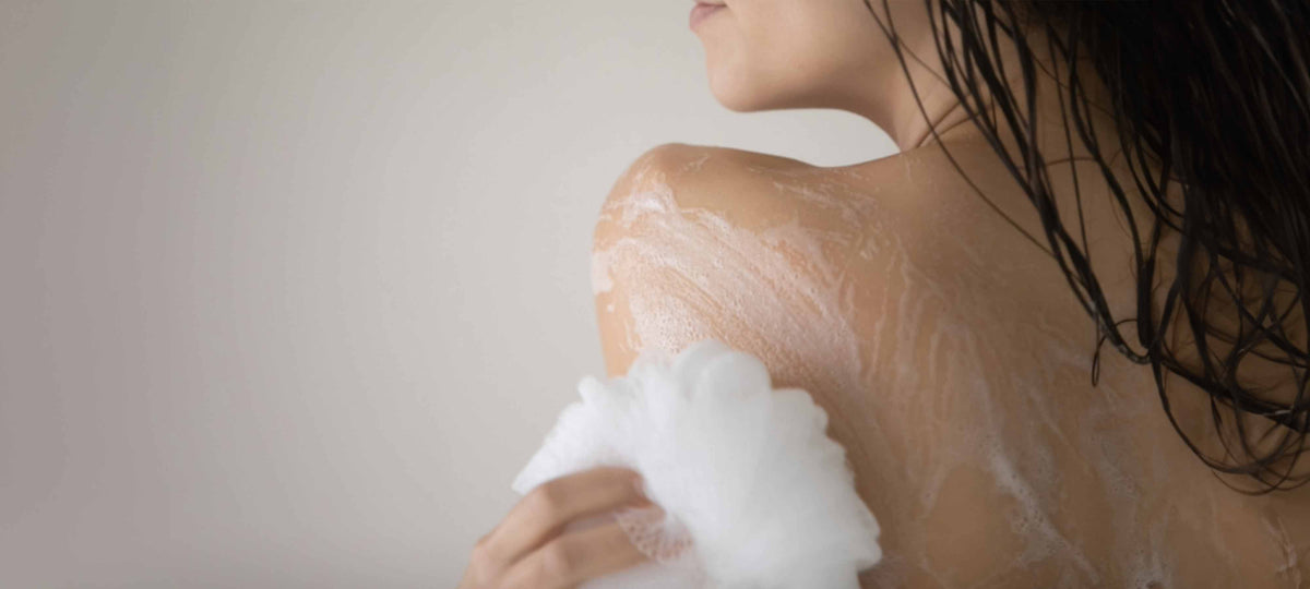 Woman applying shower gel while cleansing skin, highlighting tips for choosing the right shower gel for your skin.