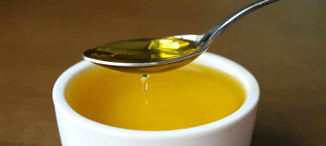 A spoon pouring fresh olive oil into a bowl, showcasing THE MIRACLE OF OLIVE OIL's versatility and health benefits.
