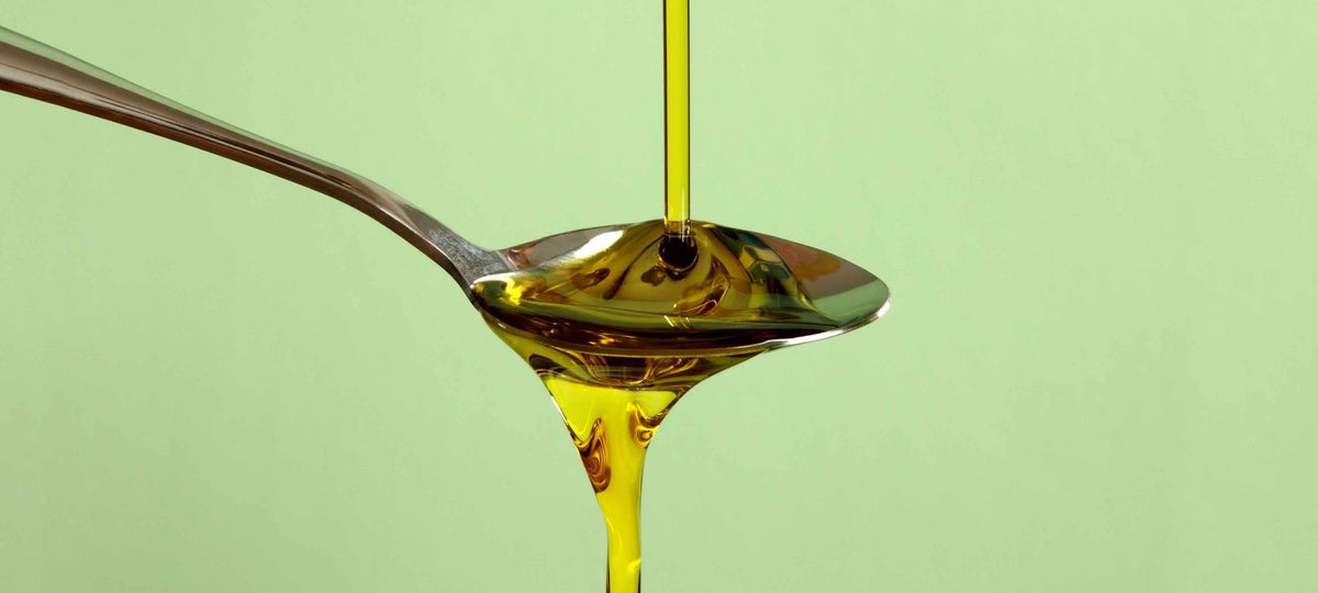 Pouring olive oil into a spoon, highlighting the color in relation to the question: What Is The Ideal Color Of Olive Oil.