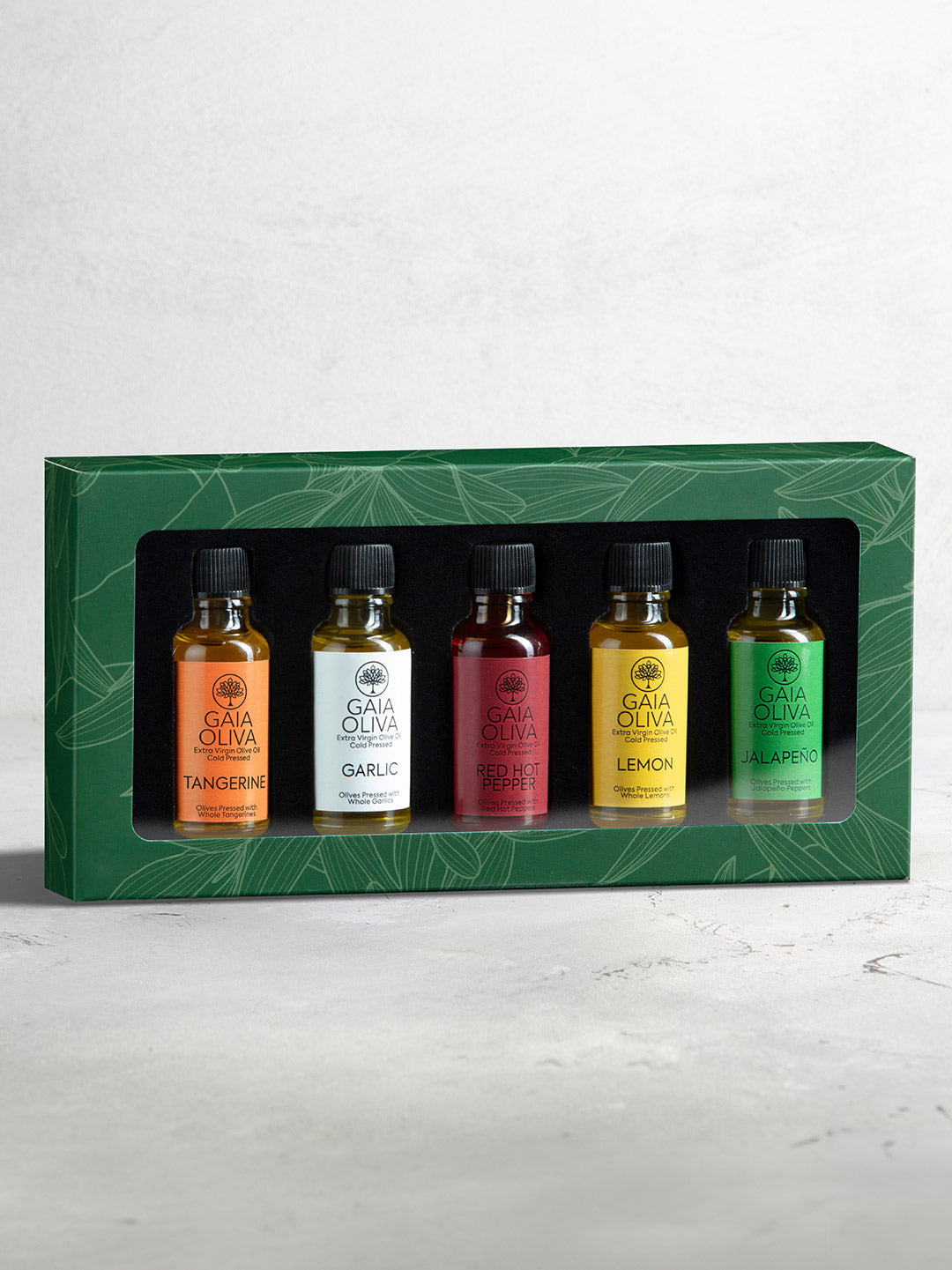 Co-Pressed Flavored Olive Oil Gift Set includes 5 bottles in different colors, displayed in a green gift box with a clear front window. The bottles are labeled Tangerine, Garlic, Hot Pepper, Lemon, and Jalapeño olive oils.