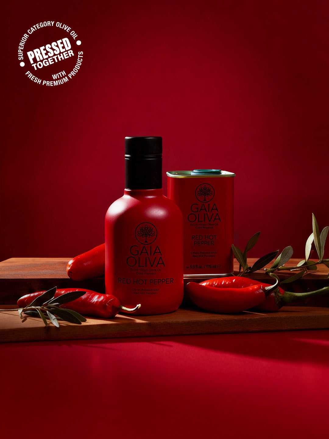 a bottle of Red Hot Pepper Extra Virgin Olive Oil and small tin with fresh pepper, red background