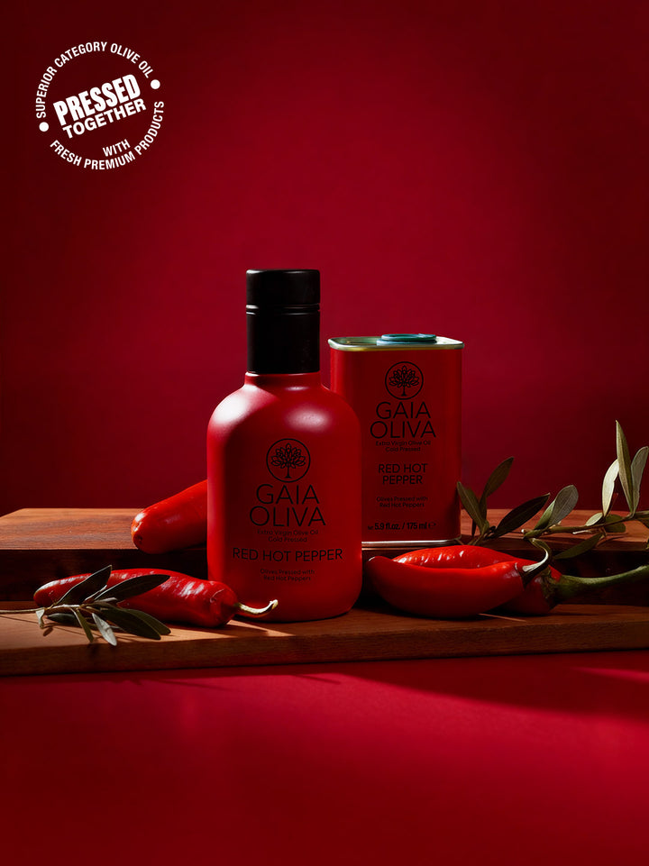 a bottle of Red Hot Pepper Extra Virgin Olive Oil and small tin with fresh pepper, red background
